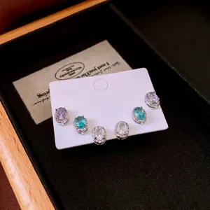 Three pairs of oval halo stud earrings in purple, blue, and white zircon on card