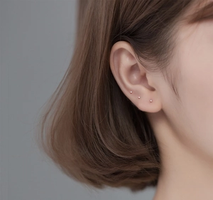 Close-up of three 999 sterling silver stud earrings worn on model's ear cartilage