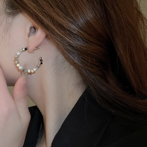 Close-up of C-shaped hoop earrings featuring alternating white pearls and silver discs