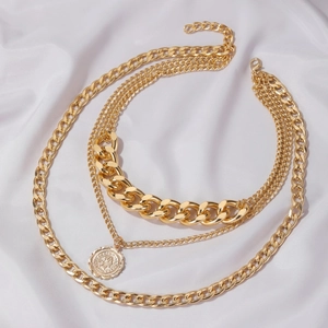 Detail view of gold layered chunky Cuban chain with coin pendant on white silk