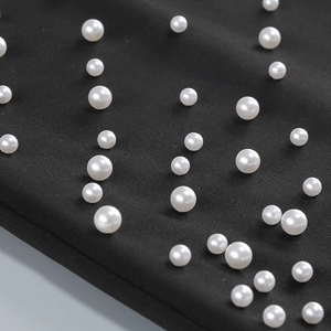 Detailed view of white pearls hand-sewn on black fabric for a strapless evening gown