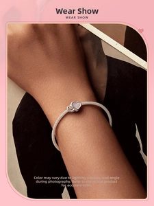 Gros plan d'un bracelet en maille argentée avec un pendentif cœur rose sur le poignet d'un modèle