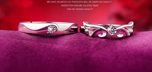Close-up of silver angel wing couple rings with zircon inlays on purple fabric background