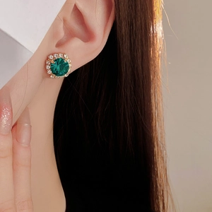 Close-up of elegant gold stud earrings with green circular stones and small diamonds
