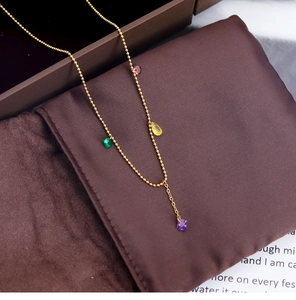 Close-up of gold beaded chain necklace with multi-colored gemstone pendants on brown fabric