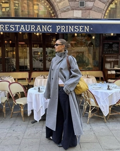 Stile street di un cappotto lungo in lana grigia con pantaloni neri a gamba larga e borsa gialla