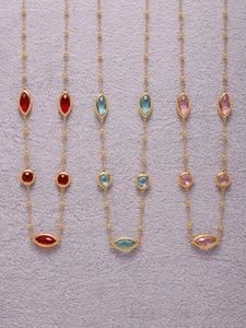 Détail des pierres colorées de taille marquise sur de fines chaînes dorées en acier