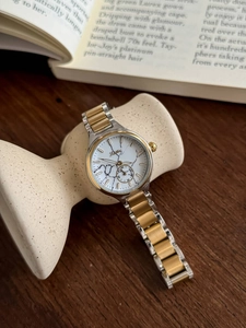 Detail of white marble dial watch with two-tone steel strap on wooden desk