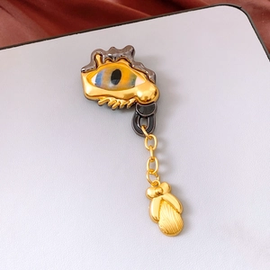 Macro shot of gold-tone vintage eye brooch with blue gradient iris and hanging relief charm