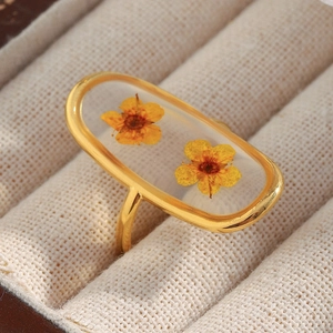 Detail of 18K gold-plated oval ring featuring delicate real yellow dried flowers in resin