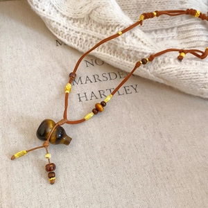 Macro detail of tiger eye gourd pendant with wooden beads on brown braided cord