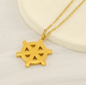 Detailed close-up of 18K gold plated dharma wheel pendant on a textured cream surface