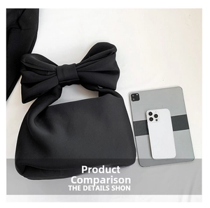 Size comparison of black bow handbag next to a tablet and smartphone on white background