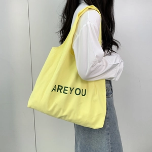Close-up of yellow canvas tote bag featuring large green AREYOU text on textured fabric