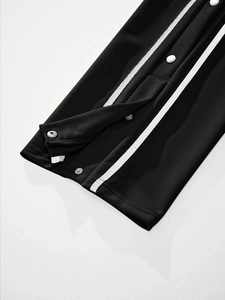Close-up of black joggers showing side white stripes and silver metal snap buttons
