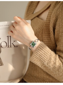 Detail of elegant silver chain watch with green square dial on a model holding a magazine