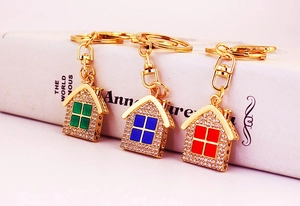 Close-up of rhinestone house keychains in green, blue, and red with gold-tone plating