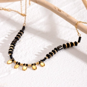 Elegant beaded necklace with black beads and gold oval pendants on a wooden branch