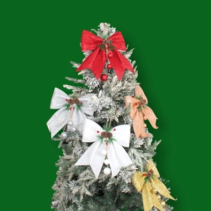 Glitter Christmas bow with pine cone and berries ornament hanging on snow-dusted tree