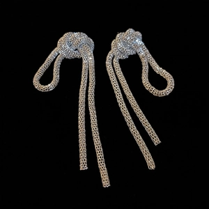 Detail of silver knot stud earrings with long mesh tassels against a black background