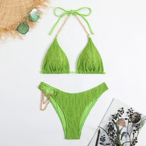 Detail of green bikini with ripple texture and decorative gold chain straps on white surface