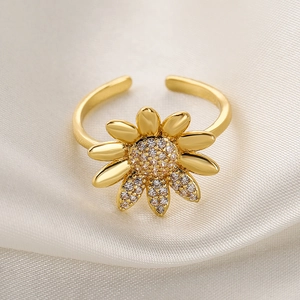 Macro detail of gold-plated flower ring with sparkling zircon pavé on beige silk