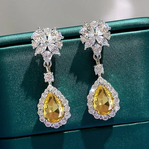 Macro shot of silver teardrop earrings featuring a pear-cut yellow gem and white zircons