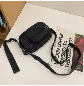 Detailed view of washed black denim crossbody bag with three practical zipper compartments