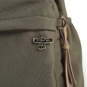 Macro detail of enamel bird badge with It Can't Rain All The Time text on nylon bag