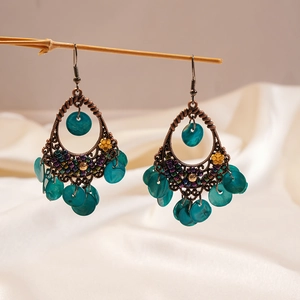 Detailed close-up of bohemian hollow bronze earrings with shell droplets on wood