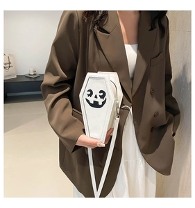 Close-up of white ghost pumpkin crossbody bag worn by a model in a stylish brown blazer
