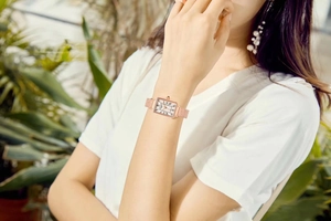 Elegant rose gold square watch with roman numerals on a female wrist in natural light