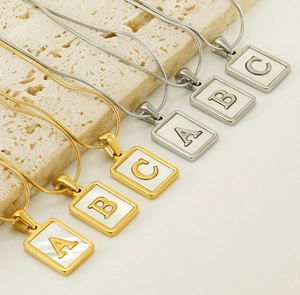 Detail view of 18K gold and silver letter pendants with shell inlay on a stone surface
