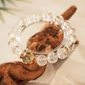 Detailed close-up of white crystal bead bracelet with a gold hollow charms on wood