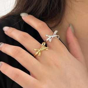 Close-up of gold and silver bow rings worn on a hand, highlighting the sleek metal finish