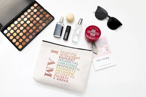Toiletry bag with inspirational text surrounded by makeup accessories on white background