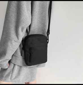 Detail of a minimalist black nylon crossbody bag styled with a casual waffle knit outfit