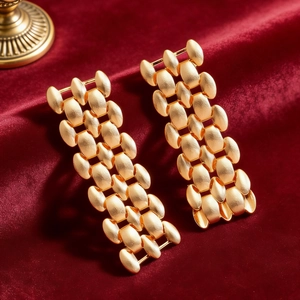 Close-up of gold rectangular mesh earrings with brushed matte texture on red velvet
