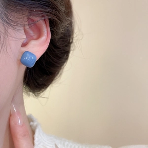 Close-up of blue square resin stud earring worn on ear showing glossy ceramic-like finish