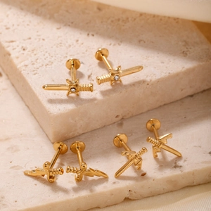 Macro detail of gold dagger stud earrings with cubic zirconia on marble surface