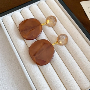 Close-up of amber resin earrings with gold leaf beads on a beige velvet jewelry tray