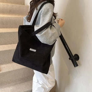 Side view of a black corduroy tote bag showing textured vertical stripes and fashion label