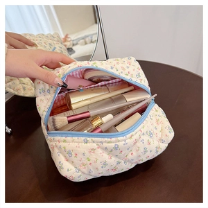 Action shot of floral quilted cotton makeup bag showing storage capacity on wooden desk