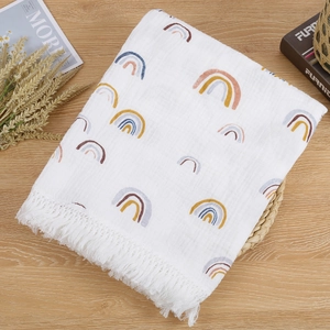 Cotton muslin baby blanket with rainbow prints and fringe tassels on a wooden table
