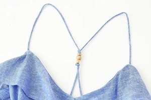 Detail of light blue linen strap dress featuring gold and wooden bead embellishments