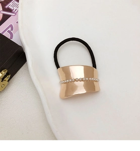 Detail of black elastic hair tie with golden metal ornament and small white pearls