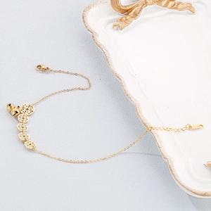 Detail of golden stainless steel anklet with lucky coin charms and small bells on a tray
