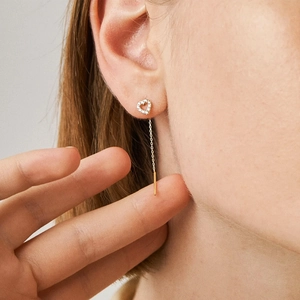 Detailed view of elegant gold heart-shaped zircon earrings with long chain tassel worn on ear