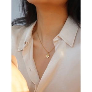 Detail of a gold-plated rose relief oval pendant necklace styled on a white silk shirt