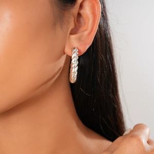Close-up profile of model wearing silver twisted hoop earrings with a metallic finish